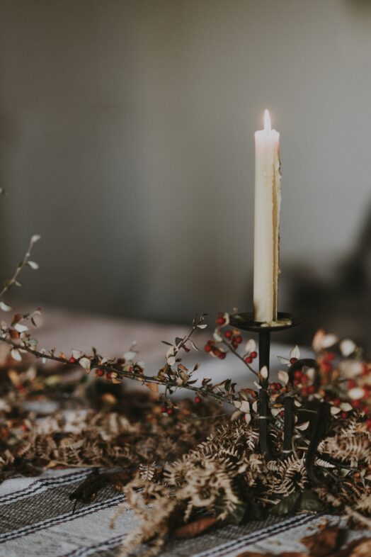 Ett tänd ljus i en ljusstake omgivet av torkade blommor.