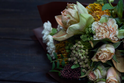 Närbild av en blomsterbukett med rosor och olika gröna växter mot en mörk bakgrund.